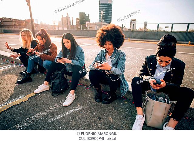 Friends sitting on kerb texting, Milan, Italy