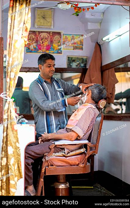 Jaisalmer, India - December 6, 2019: A barber shaving a customer in his barber shop