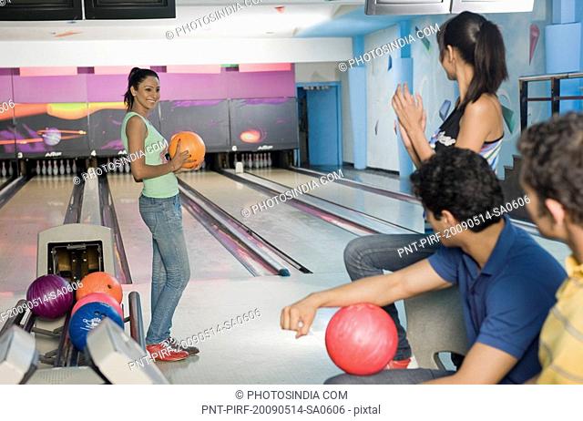 Young woman holding a bowling ball and her friends encouraging her