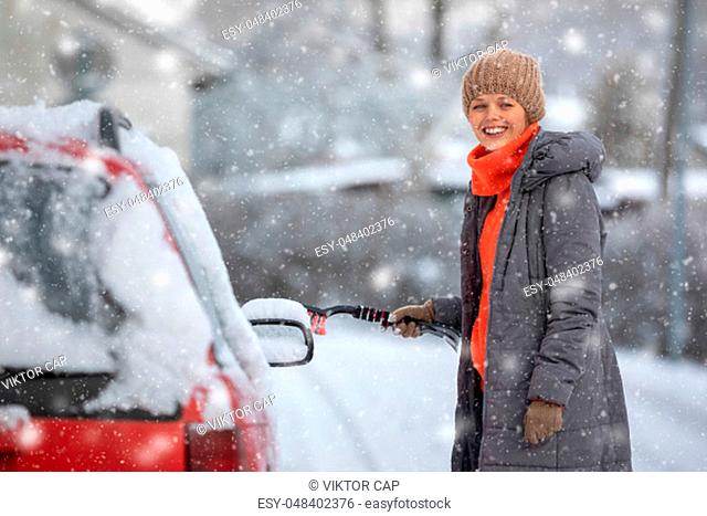 Pretty, young woman cleaning her car from snow after heavy snowstorm (color toned image)