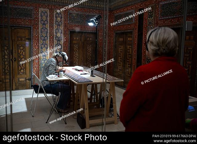 PRODUCTION - 17 October 2023, Berlin: A visitor watches a restorer in the Aleppo Room at the Pergamon Museum. From October 23
