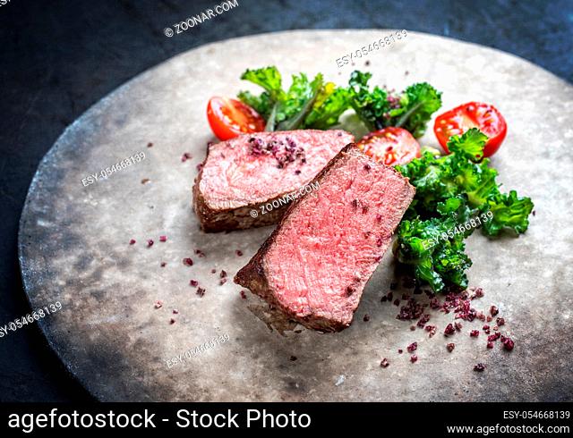 Barbecue dry aged wagyu roast beef natural sliced offered with rapini and tomatos as closeup on a modern design plate