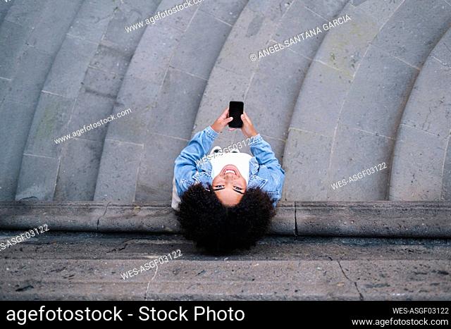 Happy young woman with mobile phone in front of wall