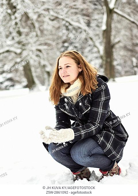 Beautiful young girl wearing a winter coat and she have a snow ball in hand, Finnish winter day on February