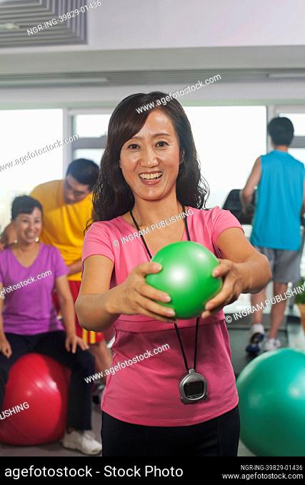 Woman holding ball on foreground, people working out in the gym on the background