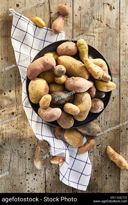 Colourful potatoes in a ceramic bowl with a tea towel on a wooden background