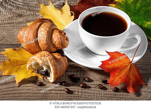 Cup of black coffee with croissants. Grains of coffee and autumn maple leaves on a wooden table