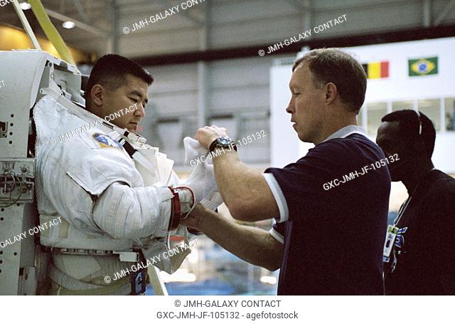 Astronaut Daniel M. Tani, STS-108 mission specialist, gets help with final touches on the training version of his Extravehicular Mobility Unit (EMU) space suit...