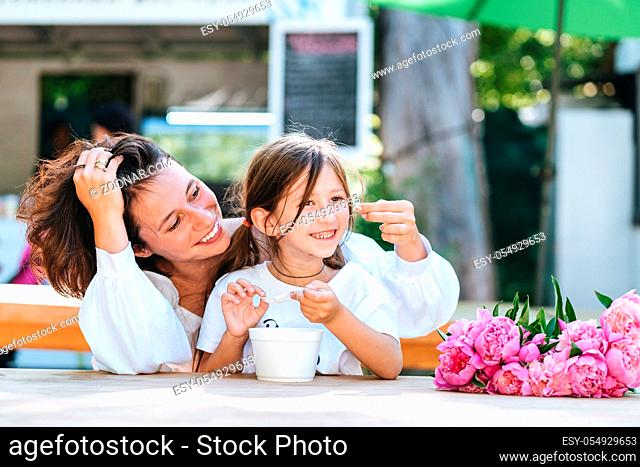 Mother and daughter are playing while sitting in a summer cafe