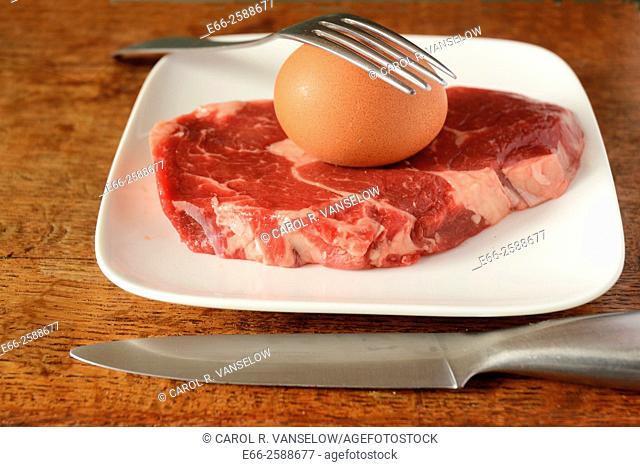 Whole brown egg in shell and ribeye steak on white plate with knife and fork. Eggs and meats are integral parts of the Paleo Diet