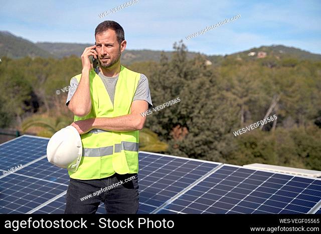 Engineer talking on mobile phone standing by solar panels