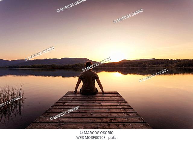 Silhouette of a man sitting on a wooden footbridge at sunset
