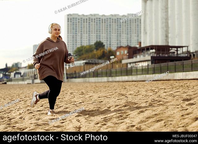 Young woman wearing headphones running at sandy beach