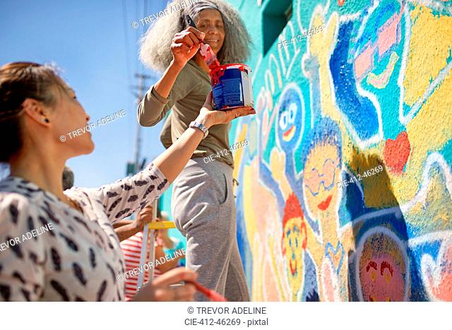 Female volunteers painting vibrant community mural on sunny urban wall