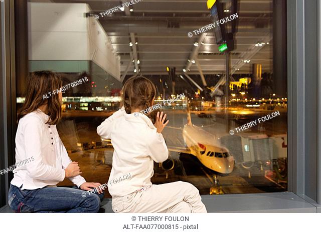 Children watch from airport terminal window as flight crew prepare commercial airplane for boarding