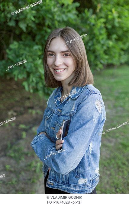 Portrait of smiling young woman with arms crossed standing at park