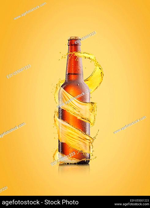 Creative spiral beer's splash around brown bottle with water droplets on a light sand yellow colored backgound, copy space. Refreshing alcohol drinks