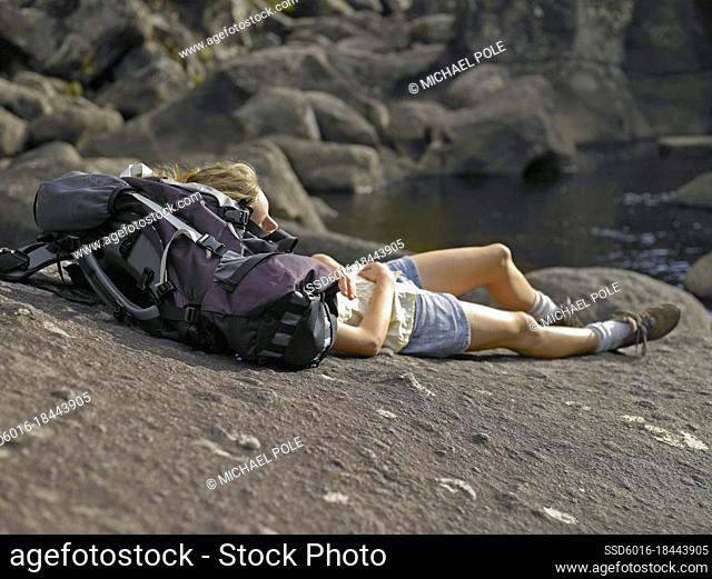 Young woman resting her head on her backpack laying on rock