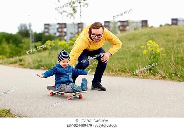 family, childhood, fatherhood, leisure and people concept - happy father and little son riding on skateboard