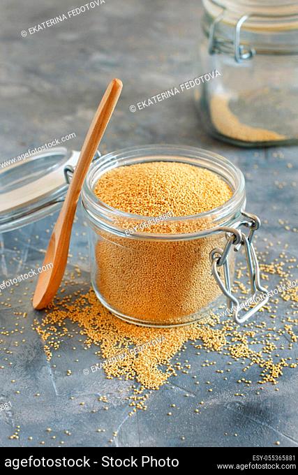 Jar of raw Amaranth Grain with a spoon on grey table close up