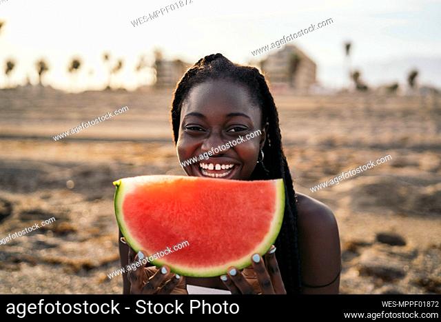 Smiling teenage girl holding watermelon slice at beach