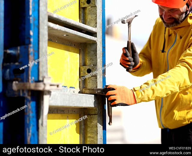 Worker hammering nail on formwork wall at construction site