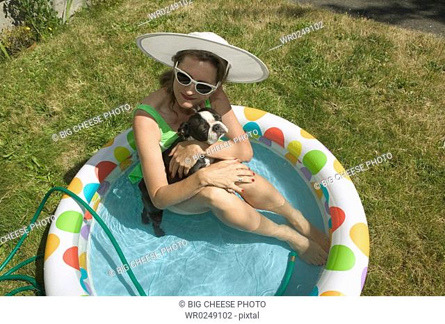 Woman sitting with her dog in backyard baby pool