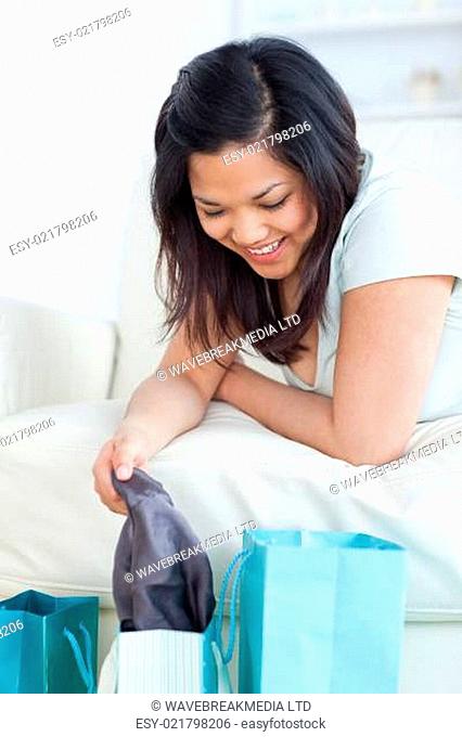 Woman lying on a couch while holding up clothes from a shopping bag in a living