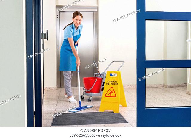 Happy Female Worker In Uniform Cleaning Floor With Mop