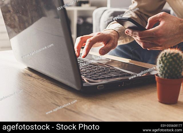 Close up of business man working on laptop computer and smartphone, sending email working from home