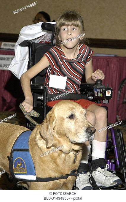 Cute little girl with disabilities operating her electric wheelchair while holding the leash of her service dog