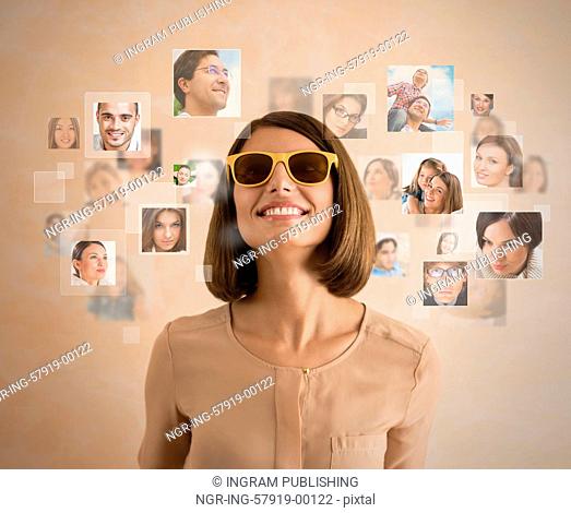 Young woman standing and smiling with many different people's faces around her. Technology social media network of friends and communication