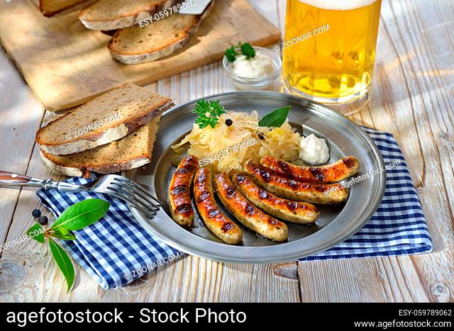 Nürnberger Rostbratwürste mit Kraut und Meerrettich traditionell auf dem Zinnteller mit Krustenbrot und einer halben Bier serviert - Fried Bavarian sausages...