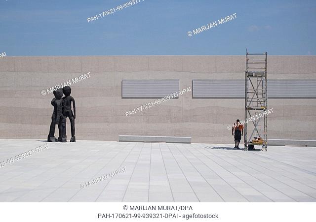 A construction worker stands under the shadow of a scaffolding, while the 2012 bronce sculpture ""BDM (Group of girls)"" stands nearby