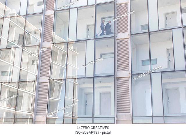 Detail of businessman and woman walking on corridor of glass fronted hotel