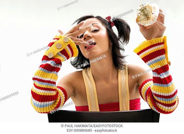 Beautiful Latina girl eating a cupcake licking her fingers and her icing covered lip, isolated