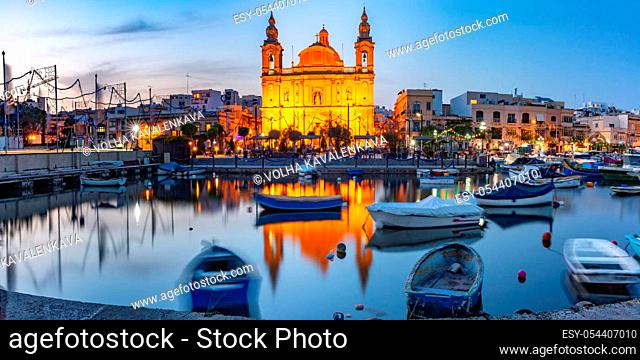 Panorama of Valletta harbour with yachts and fishing boats, Msida Parish Church of Saint Joseph at sunset, Malta