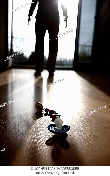 Pacifier lying on the floor in front of a silhouette of a person, symbolic image for child abuse, violence against children
