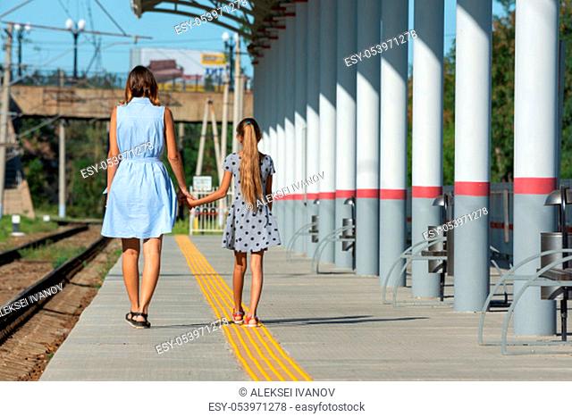 Young beautiful girl and teenage daughter walk from the camera on the empty platform of the train station