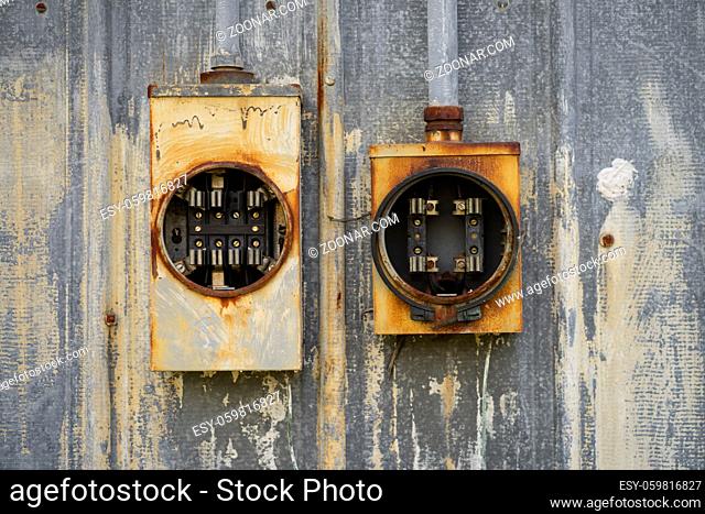 Two old electrical boxes sit empty of fuses and unused outside rusting in the elements