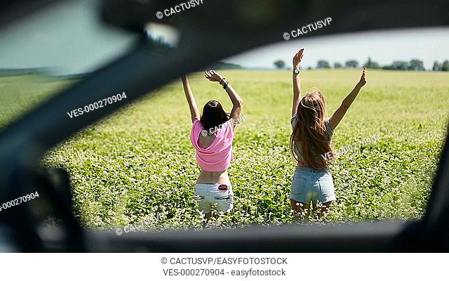 View through car window of women jumping in field