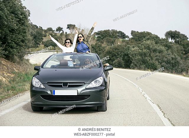 Women having fun in a convertible car on a country road