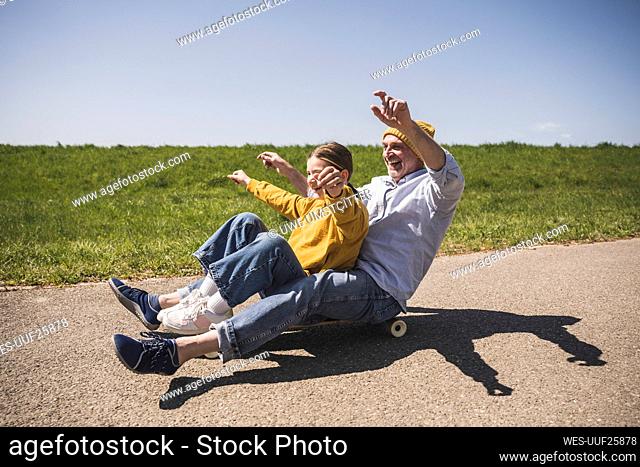 Cheerful grandfather enjoying skateboarding with granddaughter on road
