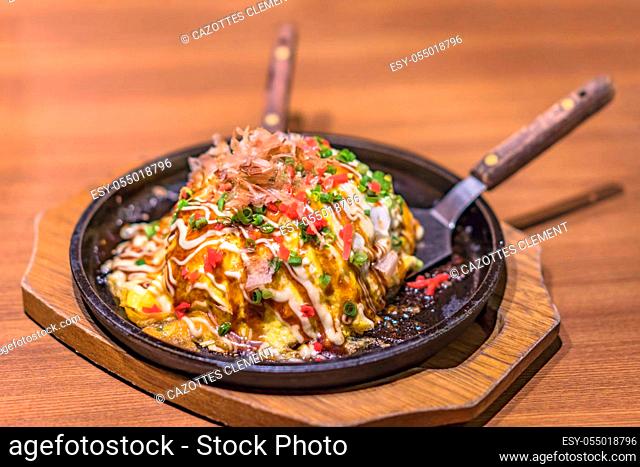 Japanese okonomiyaki covered with katsuobushi leek mayonnaise and bulldog sauce served on a hot plate with spatulas