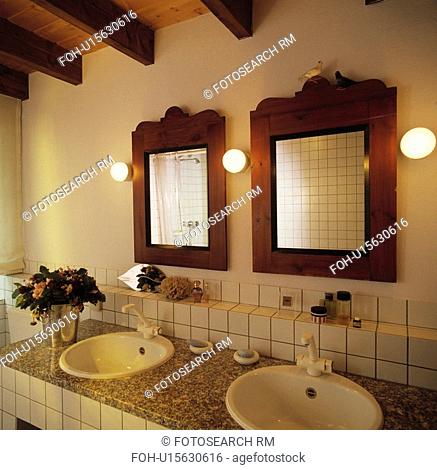 Globe lights and mahogany mirrors on wall above double white basins in granite-topped white vanity unit