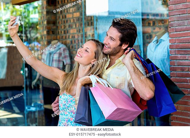 Smiling couple with shopping bags taking selfies