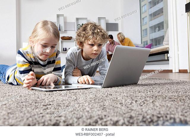 Brother and sister lying on floor using laptop and digital tablet