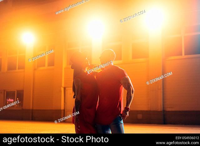 A young sexy couple lovers pose on the night street of the city. Guy and girl are close to each other