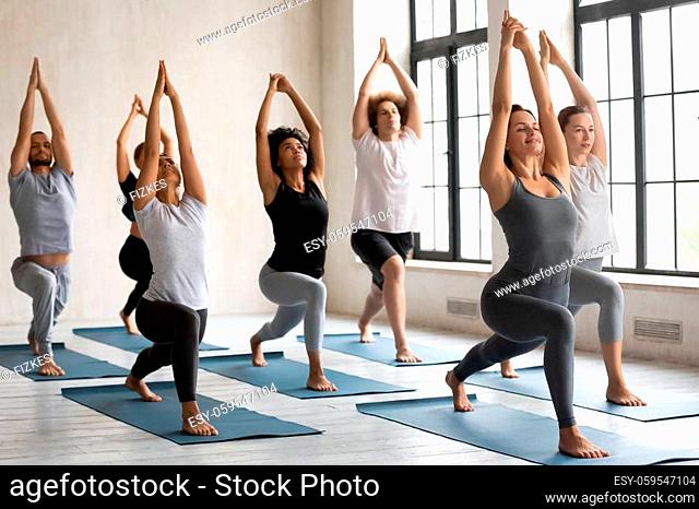 Group of active multiracial young people performing Warrior I Virabhadrasana yoga position practising exercise during session, working out in sport club