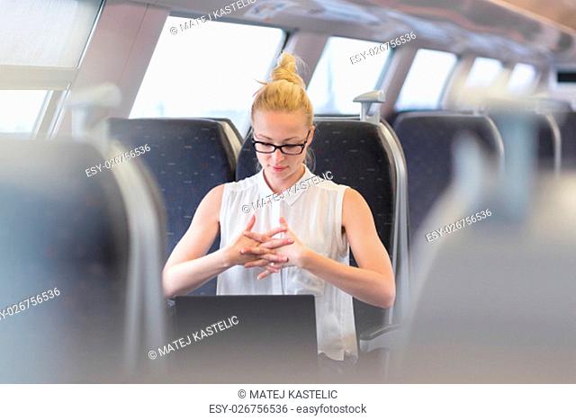 Businesswoman traveling by train, streching her fingers on her seat while working on laptop. Business travel concept